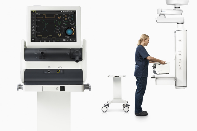 Medical professional operating a ventilator machine with a display screen showing patient data.
